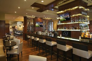 A bar area with a long counter, multiple stools, and a television screen.