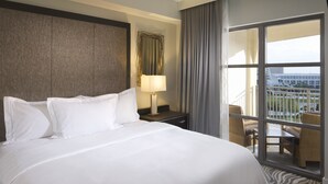 A hotel room with a large bed, a nightstand, a lamp, a window with curtains, and a view of the city.