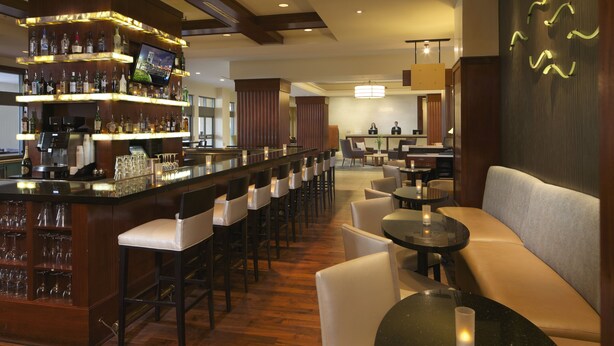 A bar area with multiple seating options, including bar stools and round tables, and a television mounted on the wall.