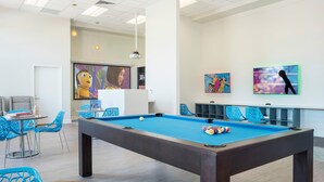 A pool table with a blue felt surface, surrounded by blue chairs and a chessboard.