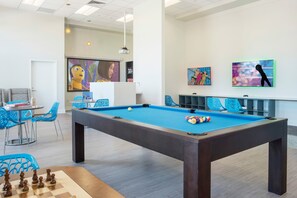 A pool table with a blue felt surface, surrounded by blue chairs and a chessboard.