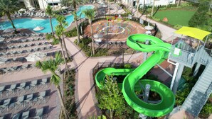 A resort with a pool, lounge chairs, a water slide, and a playground.