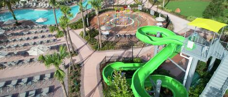 A resort with a pool, lounge chairs, a water slide, and a playground.