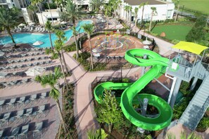 A resort with a pool, lounge chairs, a water slide, and a playground.