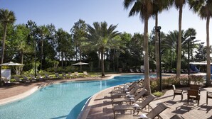A swimming pool with lounge chairs and umbrellas, surrounded by palm trees.