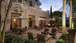 An outdoor patio area with seating and tables, a building with balconies, and a Ferris wheel in the background. - Las Palmeras, a Hilton Grand Vacations Club - 2 Bedroom Lock Off - 2LK (Orlando)