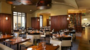 A spacious restaurant with multiple dining tables and chairs, wooden paneling, and a modern chandelier.