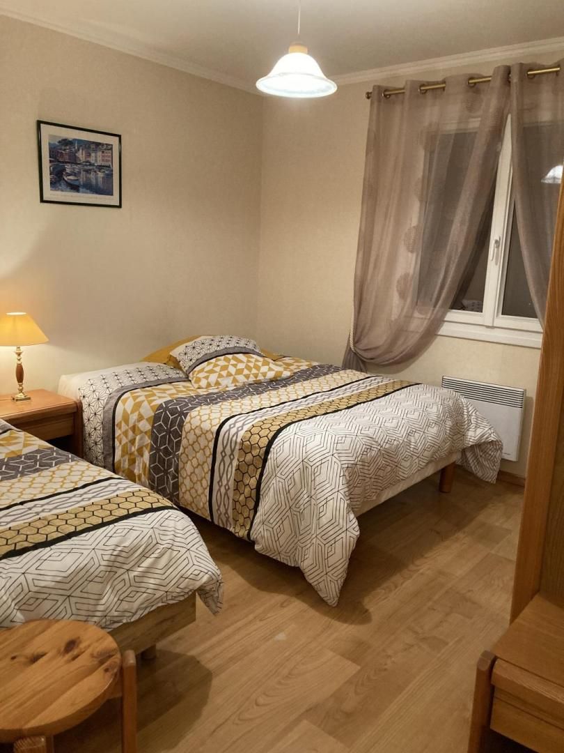 Un dormitorio con dos camas, una mesita de noche con lámpara, una ventana con cortinas y un cuadro en la pared.