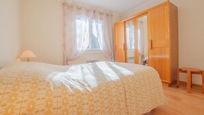 Un dormitorio con cama, armario de madera, una mesita y una ventana con cortinas.