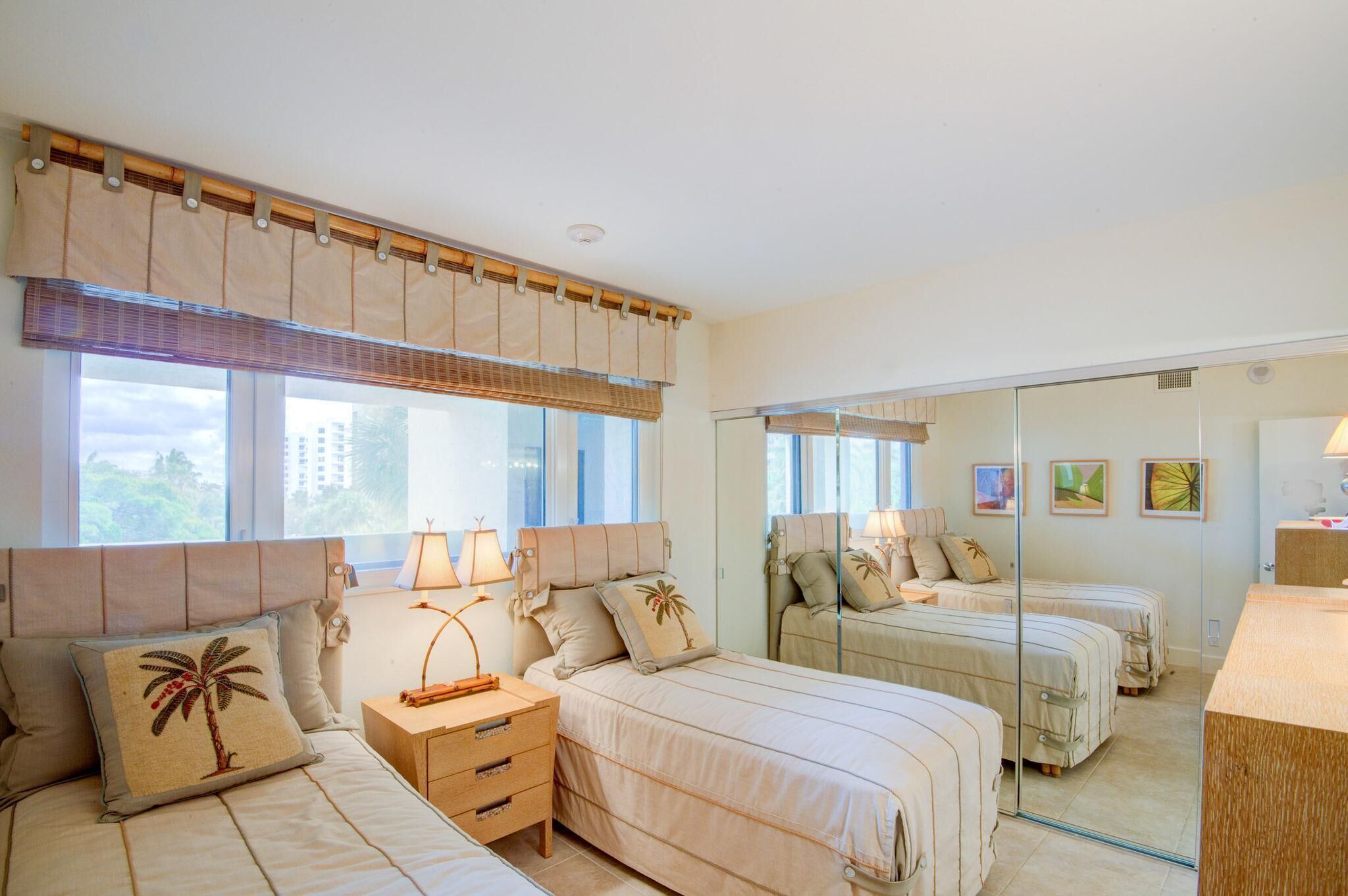 A bedroom with two beds, a nightstand, a mirror, and a window with blinds.
