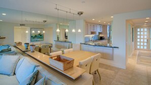 A modern kitchen with a dining area, featuring a long wooden table, white chairs, and pendant lighting. - Beachplace 7 - 202 by FGC (Longboat Key)