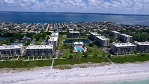 An aerial view of a coastal resort with multiple high-rise buildings, a central pool area, and a beach with boats. - Beachplace 7 - 202 by FGC (Longboat Key)