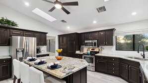 Una cocina moderna con armarios oscuros, electrodomésticos de acero inoxidable, encimera de granito y ventilador de techo.
