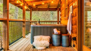 A wooden cabin with a wooden deck, a hot tub, and a fluffy dog.