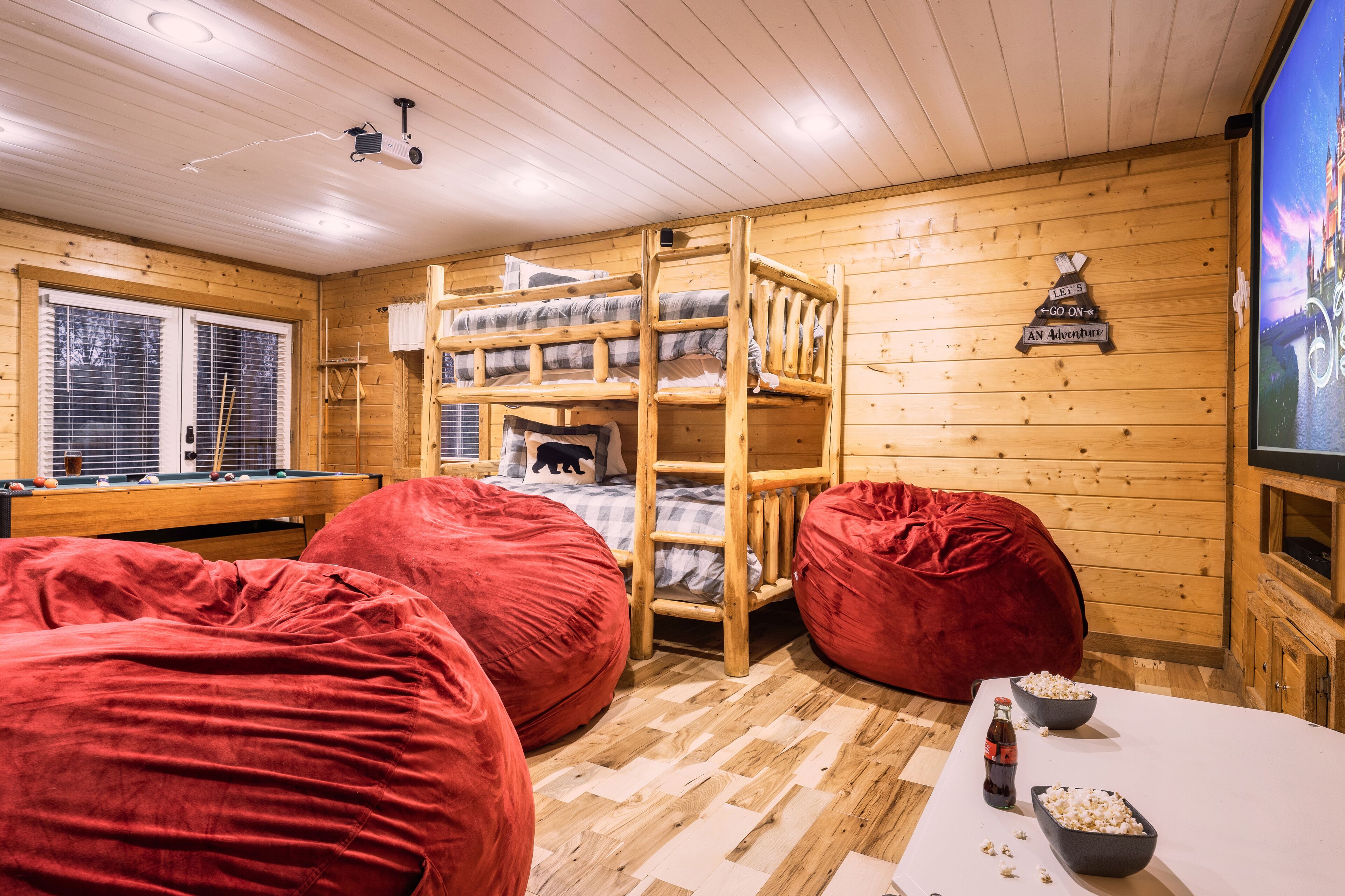 A cozy cabin room with bunk beds, a pool table, red bean bags, and a television.