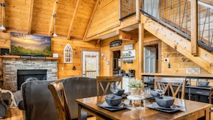 A cozy cabin interior with a stone fireplace, wooden dining table, and comfortable seating.