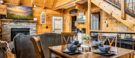 A cozy cabin interior with a stone fireplace, wooden dining table, and comfortable seating.