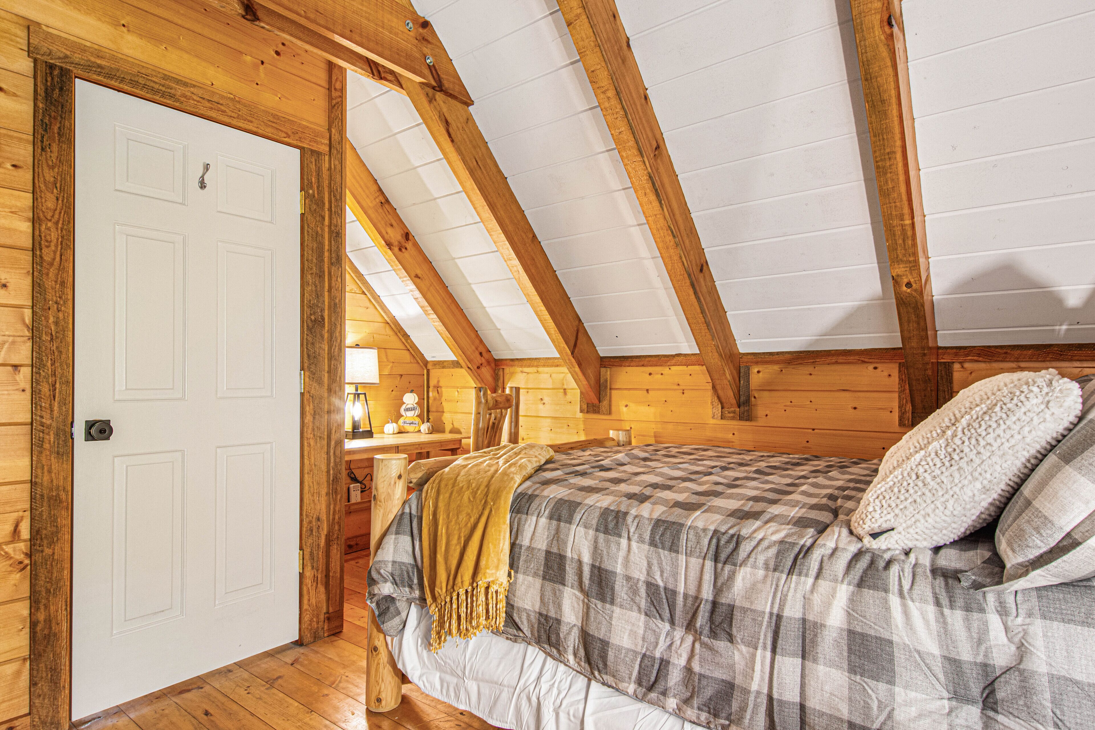 A wooden room with a bed, a white door, and a wooden ceiling.