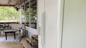 Un espacio al aire libre techado con un refrigerador blanco, cubierta de madera, asientos exteriores y un ventilador.