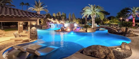 A swimming pool with a waterfall feature, surrounded by palm trees and a stone patio.