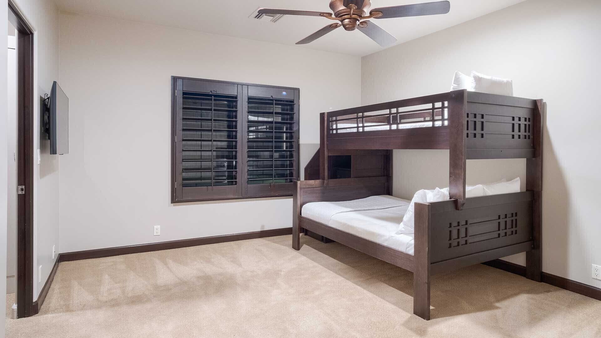 A bedroom with a bunk bed, a ceiling fan, a window with blinds, and a carpeted floor.