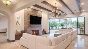 A spacious living room with a stone fireplace, a large flat-screen TV, and a chandelier. - 7BR Luxury Oasis w/ Relaxing Lazy River, Basketball, Full Gym & Private Theater (Paradise Valley)