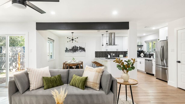 Een moderne woonkamer met een grijze bank, een eettafel en een keuken met witte kasten en roestvrijstalen apparatuur.