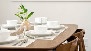 Een eettafel gedekt met witte borden, kommen en bestek, met een stadslandschap als muurdecoratie op de achtergrond.