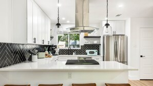 Een moderne keuken met een centraal eiland, barstoelen, roestvrijstalen apparatuur en een zwart-wit achterwand.