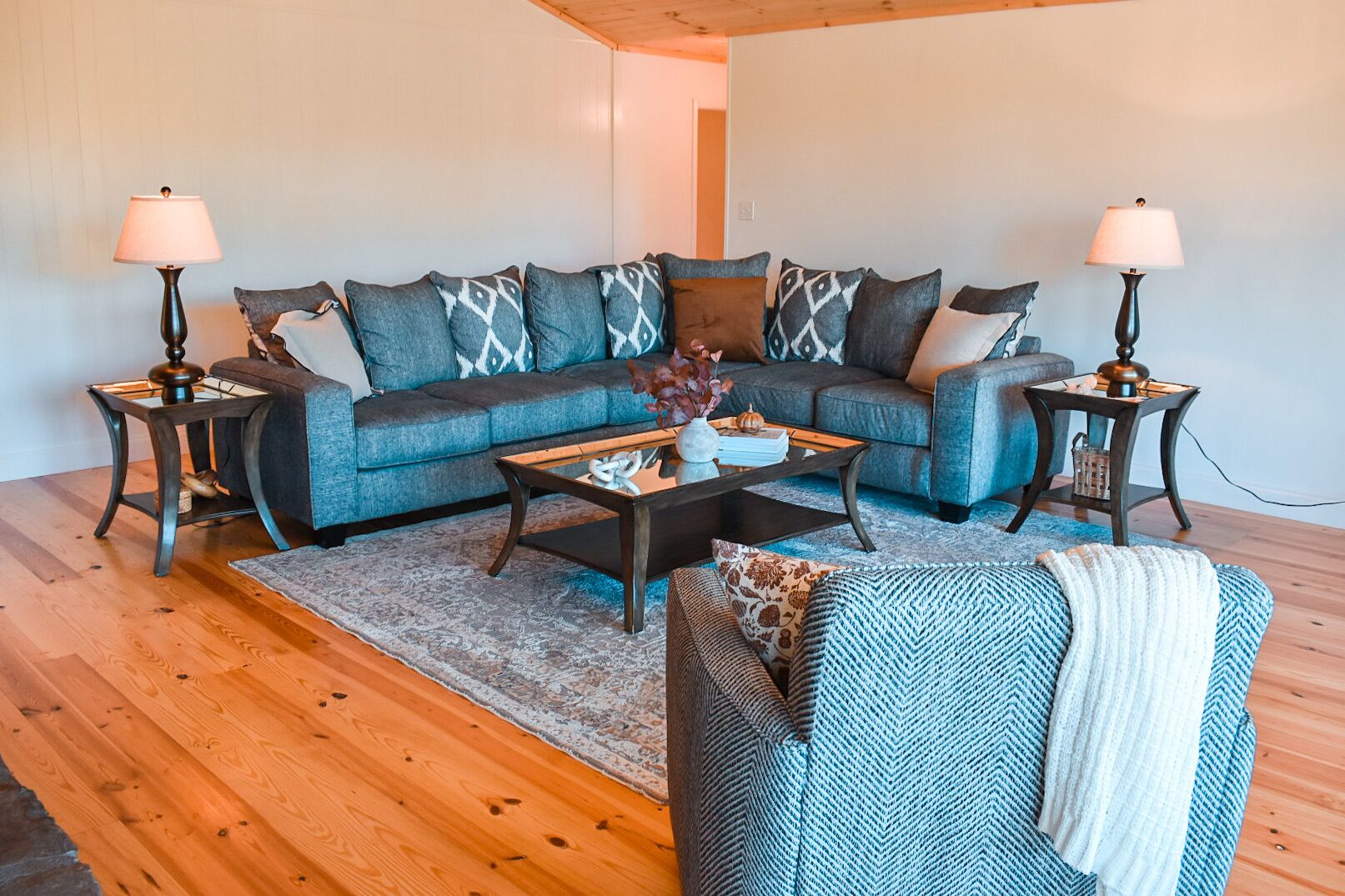 A modern living room with a sofa set, two side tables, a coffee table, and a patterned rug.