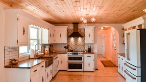 Cocina con techo de madera, armarios blancos, estufa y refrigerador.