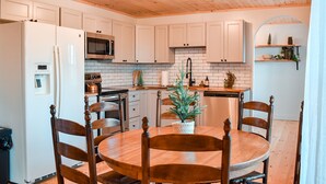 Una cocina con armarios blancos, una mesa de comedor de madera y sillas.