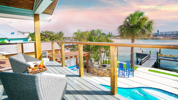 A wooden deck with wicker chairs, a small pool, and a view of the water. - Waterfront 5-bed 4 bath with heated pool BTR 2030 (Indian Rocks Beach)