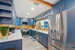 A modern kitchen with blue cabinets, stainless steel appliances, and a wooden accent wall. - Waterfront 5-bed 4 bath with heated pool BTR 2030 (Indian Rocks Beach)