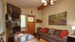 Ein gemütliches Wohnzimmer mit Kamin, einer Essecke mit Tisch für zwei Personen und einem bequemen Sofa mit roten Kissen.
