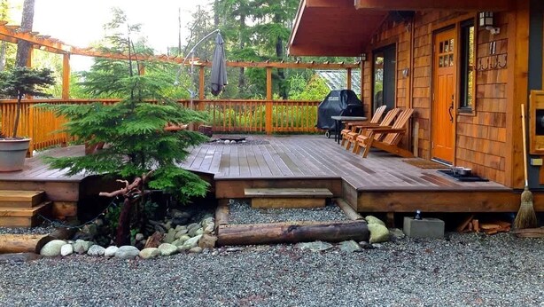 Eine Holzblockhütte mit Terrasse, Sitzgelegenheiten im Freien und einem Grill.