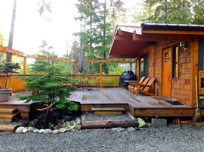 A wooden cabin with a deck, outdoor seating, and a barbecue grill.