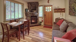 Ein Wohnzimmer mit Kamin, eine Essecke mit Tisch für zwei Personen und eine Couch mit Kissen.