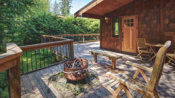 A wooden deck with a fire pit, outdoor seating, and a view of the surrounding forest.