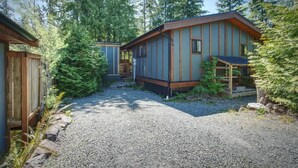 A cabin with a gravel driveway, surrounded by dense forest.