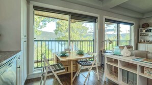 A kitchen with a wooden table, two chairs, a white cabinet, and a view of a balcony with greenery.