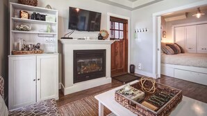 A living room with a fireplace, a television, and a bed in the adjacent room.