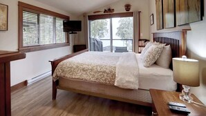 Un dormitorio con una cama grande, televisor, ventana con persianas y vistas al exterior.