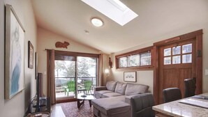 Un salón espacioso con un sofá grande, una mesa de centro y un comedor con mesa y sillas. Hay un ventanal amplio que proporciona luz natural y vistas al exterior.