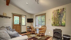 A cozy living room with a sofa, a coffee table, a fireplace, and a dining area with chairs and a table. - Explorers Retreat  Private Sauna - Pet Friendly (Port Renfrew)