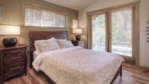 A bedroom with a large bed, wooden headboard, two bedside tables with lamps, and a window with blinds. - Explorers Retreat  Private Sauna - Pet Friendly (Port Renfrew)