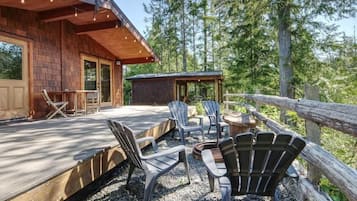 A wooden deck with Adirondack chairs and a fire pit, surrounded by a wooden fence and trees.