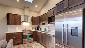 A modern kitchen with dark wood cabinets, stainless steel appliances, and a skylight. - Amazing Marina & Oceanfront View - Pet Friendly - Sleeps 6 (Port Renfrew)