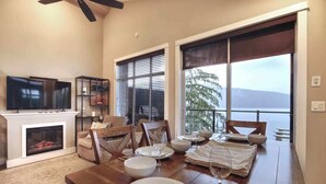 A dining area with a wooden table set for four, a fireplace, and a large window with a view. - Amazing Marina & Oceanfront View - Pet Friendly - Sleeps 6 (Port Renfrew)
