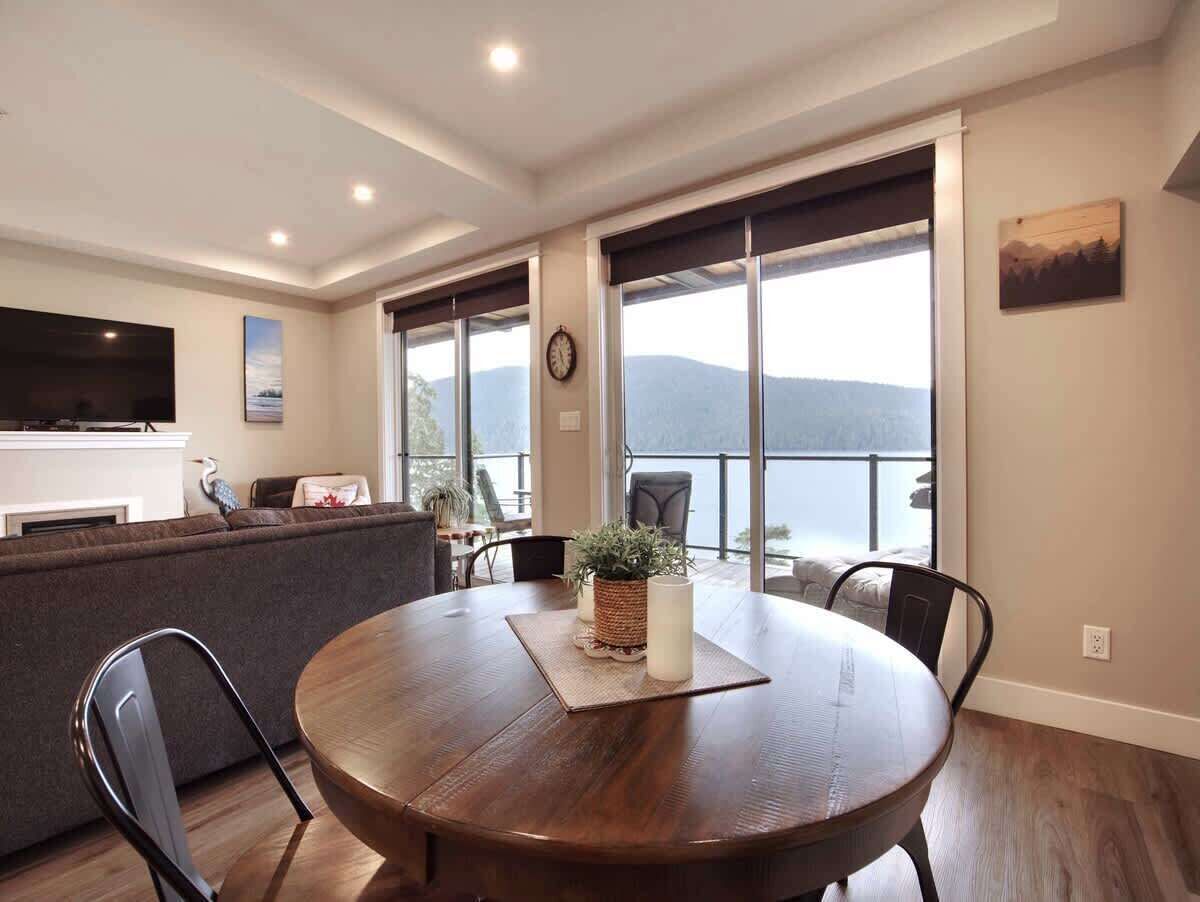 A modern living room with a round wooden table, a sofa, and a large window offering a view of the mountains.